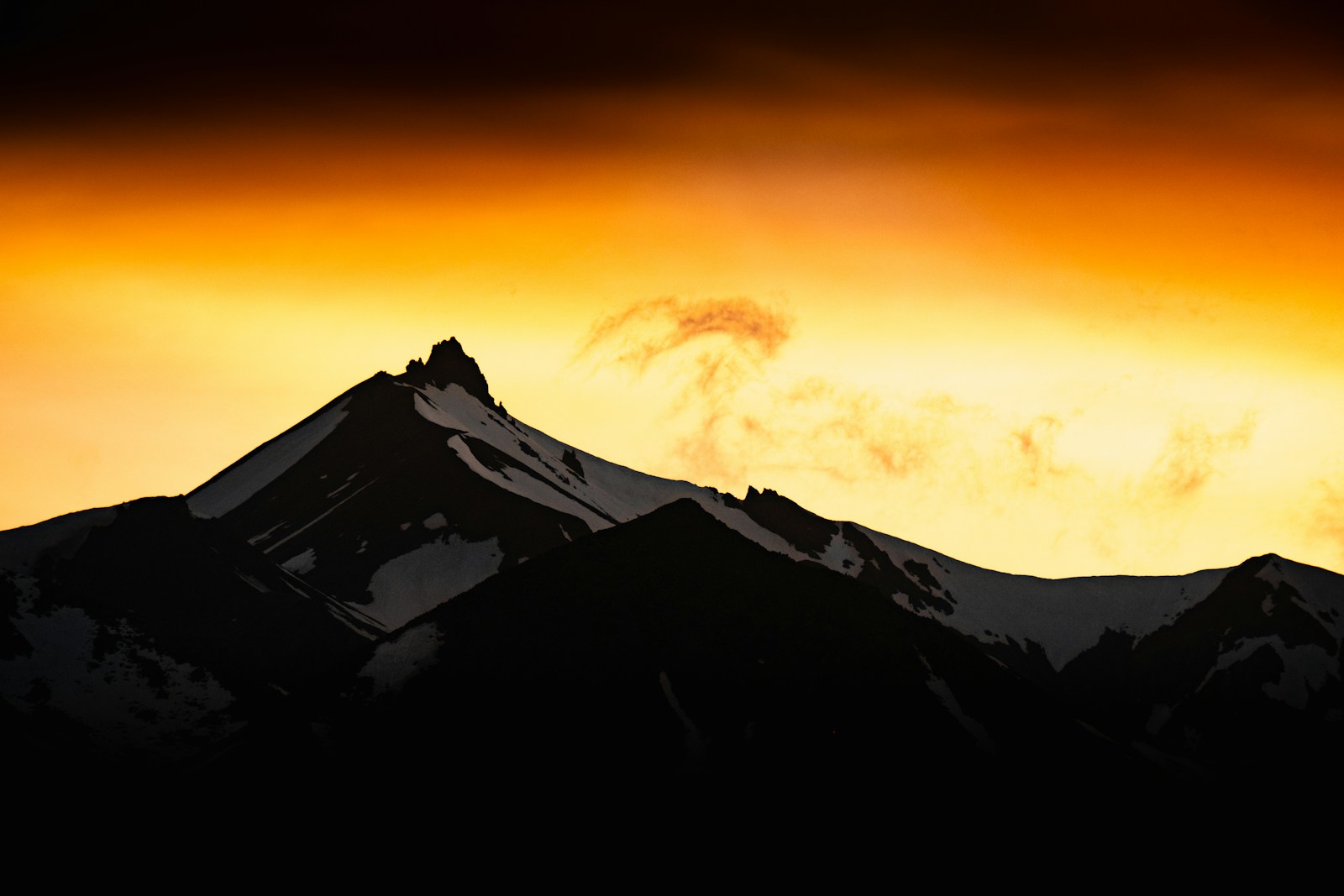 A mountain is silhouetted against an orange sky