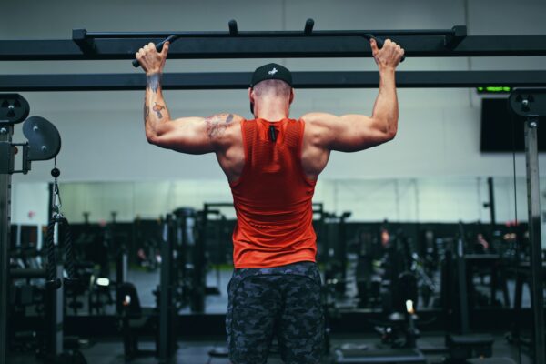 man in red tank top and black shorts holding black and silver barbell