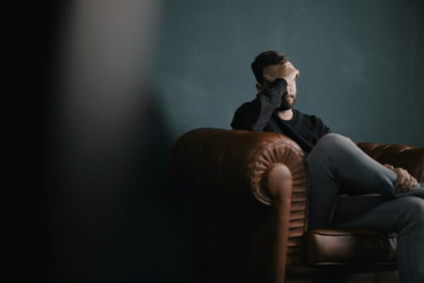 a man holds his head while sitting on a sofa